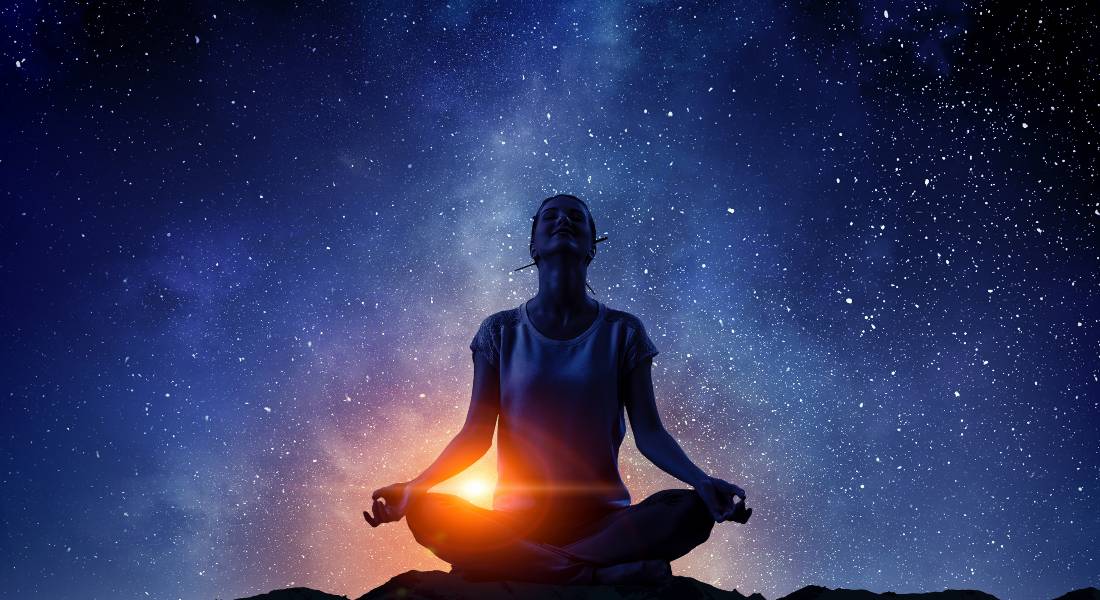 Person meditating under a starry sky with a glowing, bright orb of energy.
