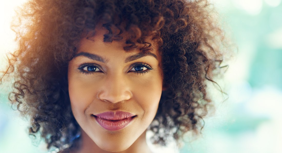 Woman with a smile and curly hair against a blurred sunlight background.