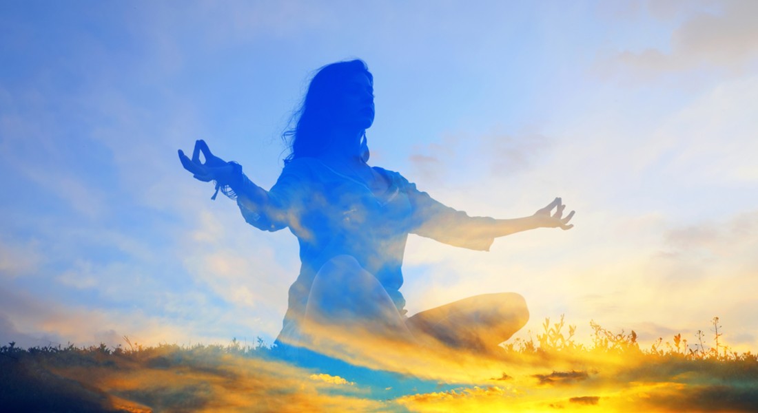 Silhouette of a person meditating on spiritual growth with a sunrise in the background.