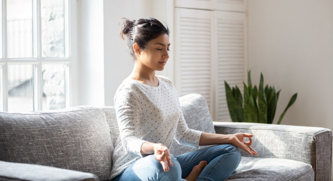 Woman meditating comfortably on a couch indoors, representing the ease and flexibility of accepting distant attunements from Blissful Light.