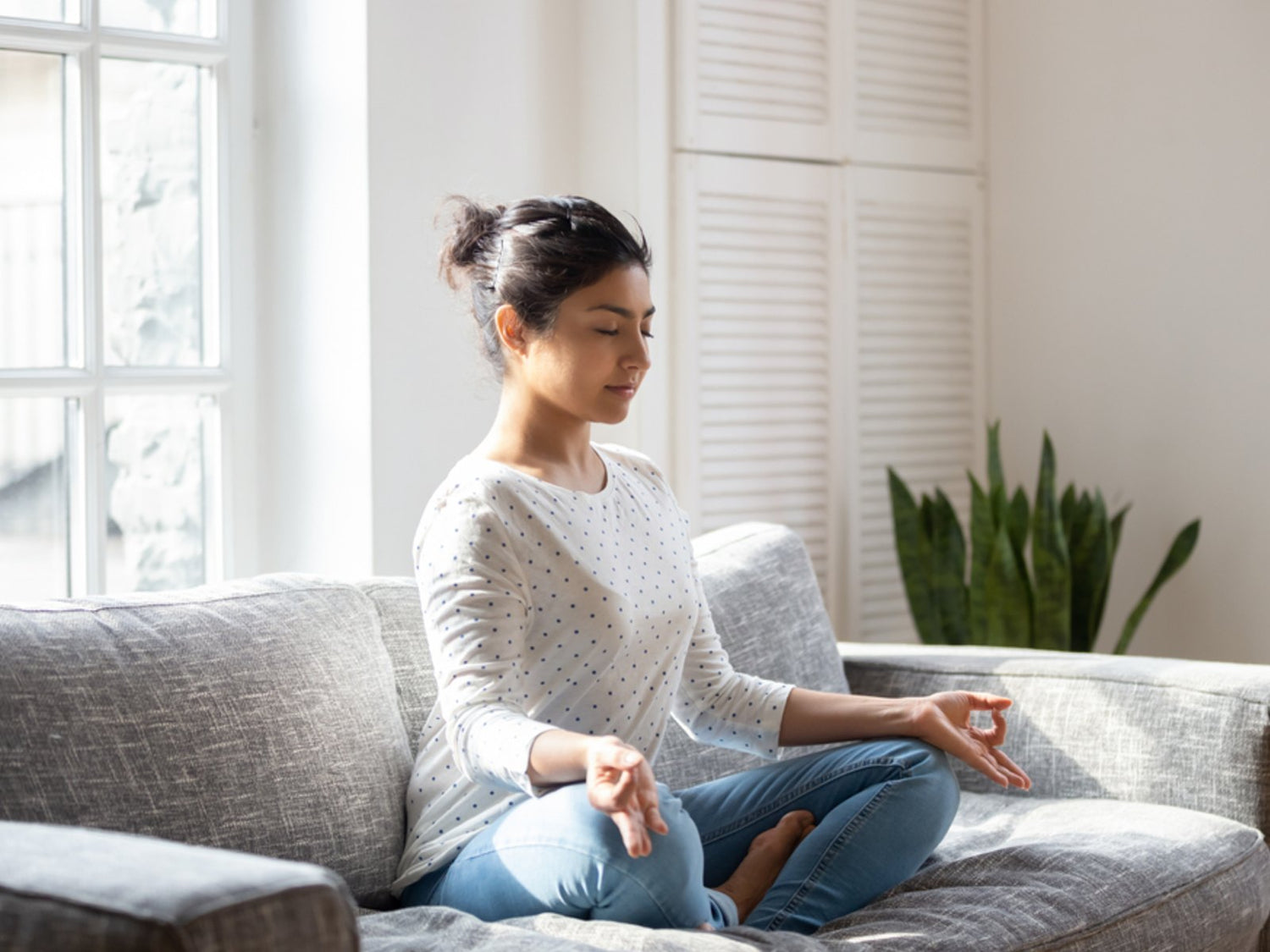 Woman meditating comfortably on a couch indoors, representing the ease and flexibility of accepting distant attunements from Blissful Light.