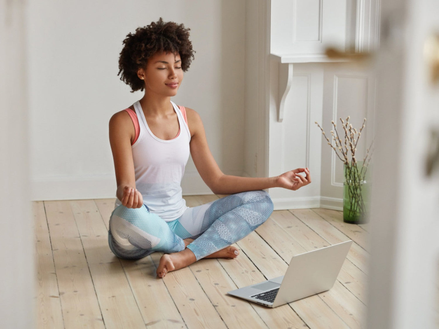 Woman meditating calmly on a wooden floor beside an open laptop, symbolising self-reflection for distant energy healing.