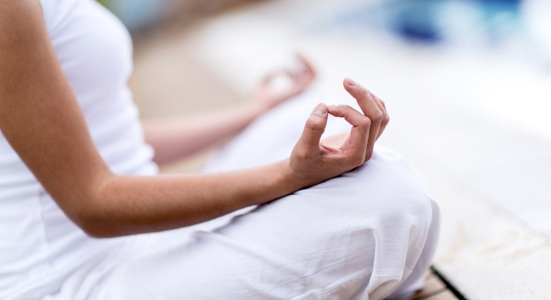 Person in white outfit meditating with hands in a prayer position on a blurred background.
