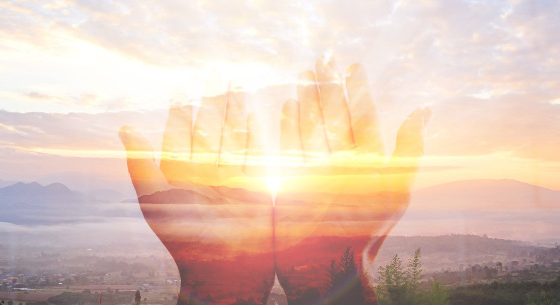 Persons hands in a scenic landscape with a bright light source creating a double exposure effect.