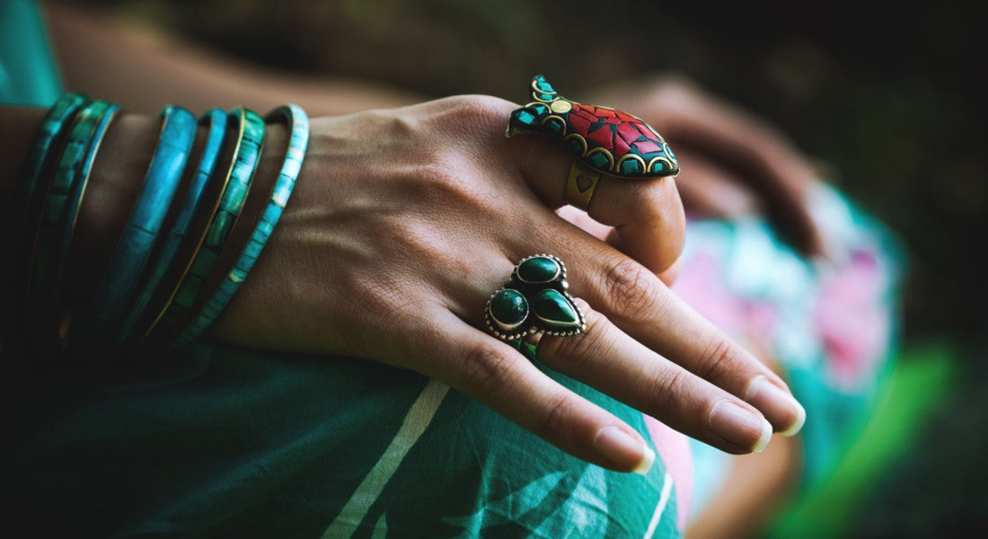 Close-up of hands wearing green jewellery with a blurred background.