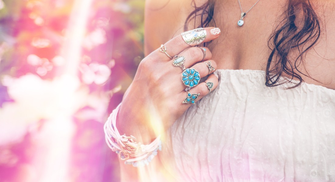 Person wearing multiple turquoise rings on a blurred pink light outdoor background