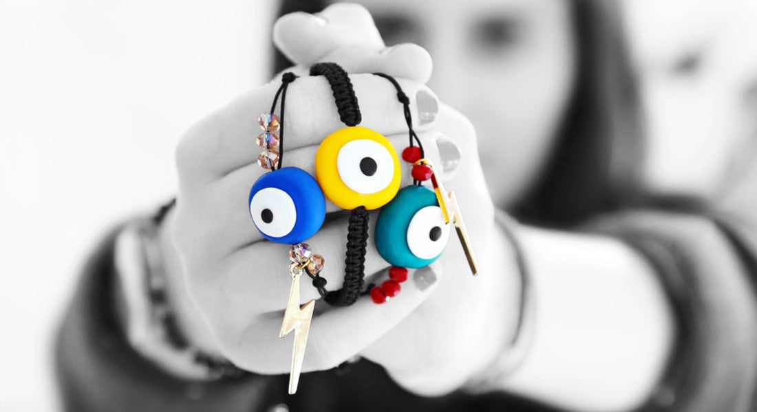 Colourful evil eye charms on a black cord held by a hand against a blurred background.