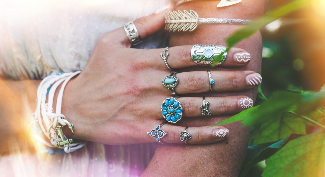 Hand with multiple rings and bracelets against a blurred natural background.
