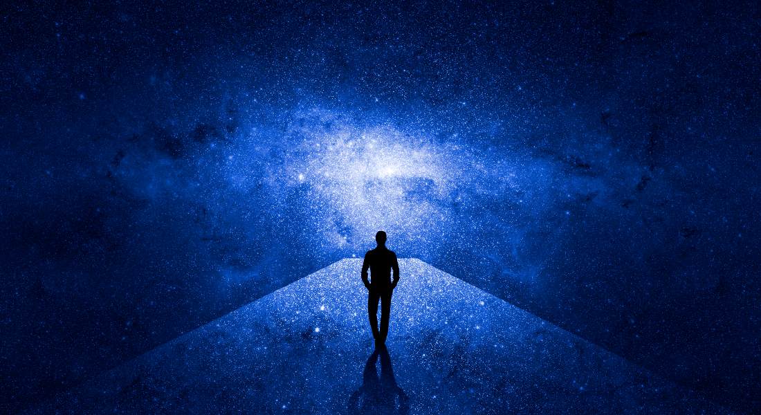 Person standing on a platform looking at a starry night sky with a bright light source.