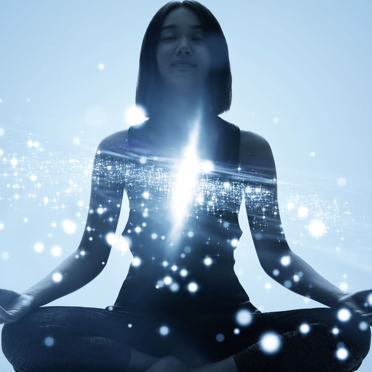 Silhouette of a young woman meditating, with heart centre illuminated by an intense burst of white light and sparkling.