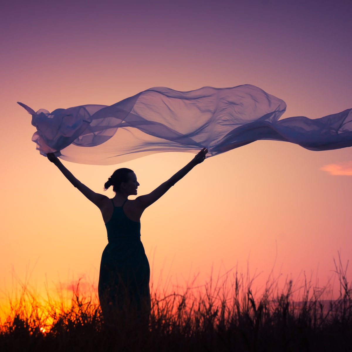 Woman holding a flowing fabric against a sunset sky symbolising elemental air.