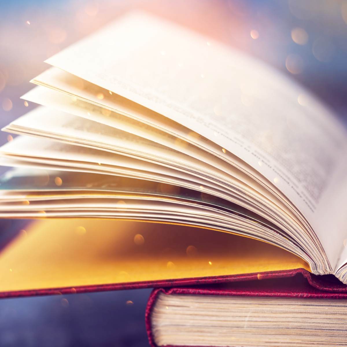 Close-up of a large, opened book with pages illuminated by a warm, ethereal light and golden bokeh sparkles.