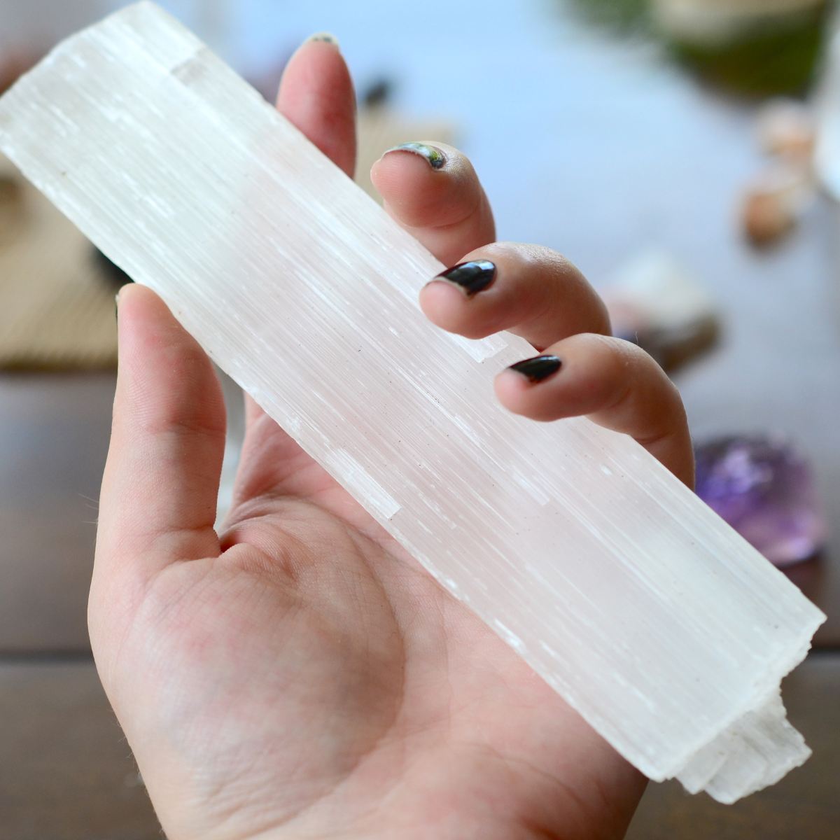 A hand gently holding a long, rectangular piece of white selenite crystal, representing angelic selenite protection.
