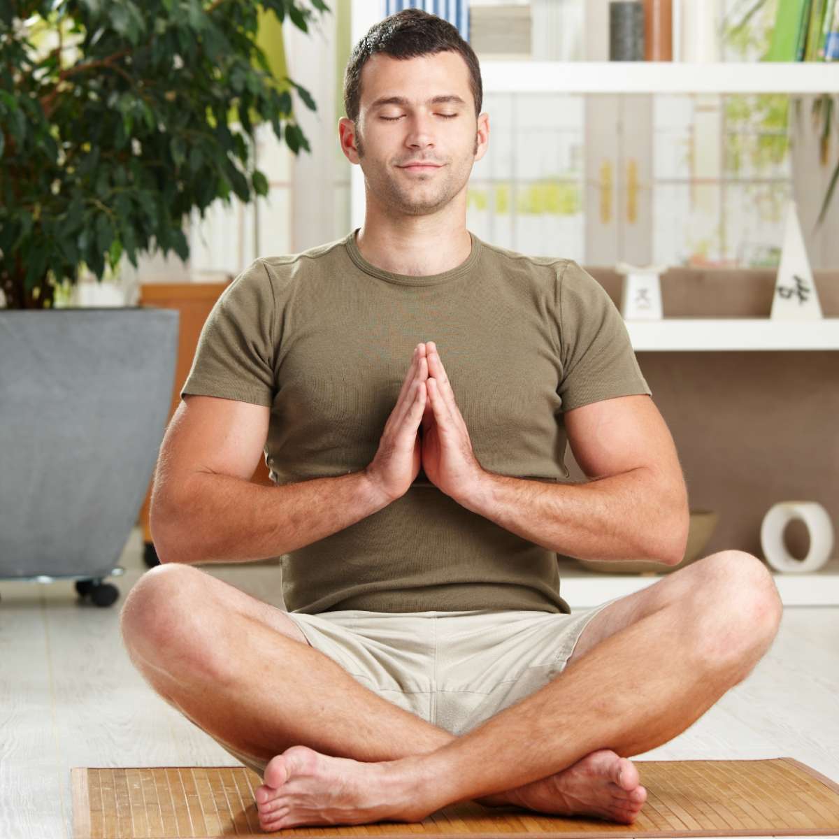 Man peacefully meditating in a living room with plants and furniture in the background.