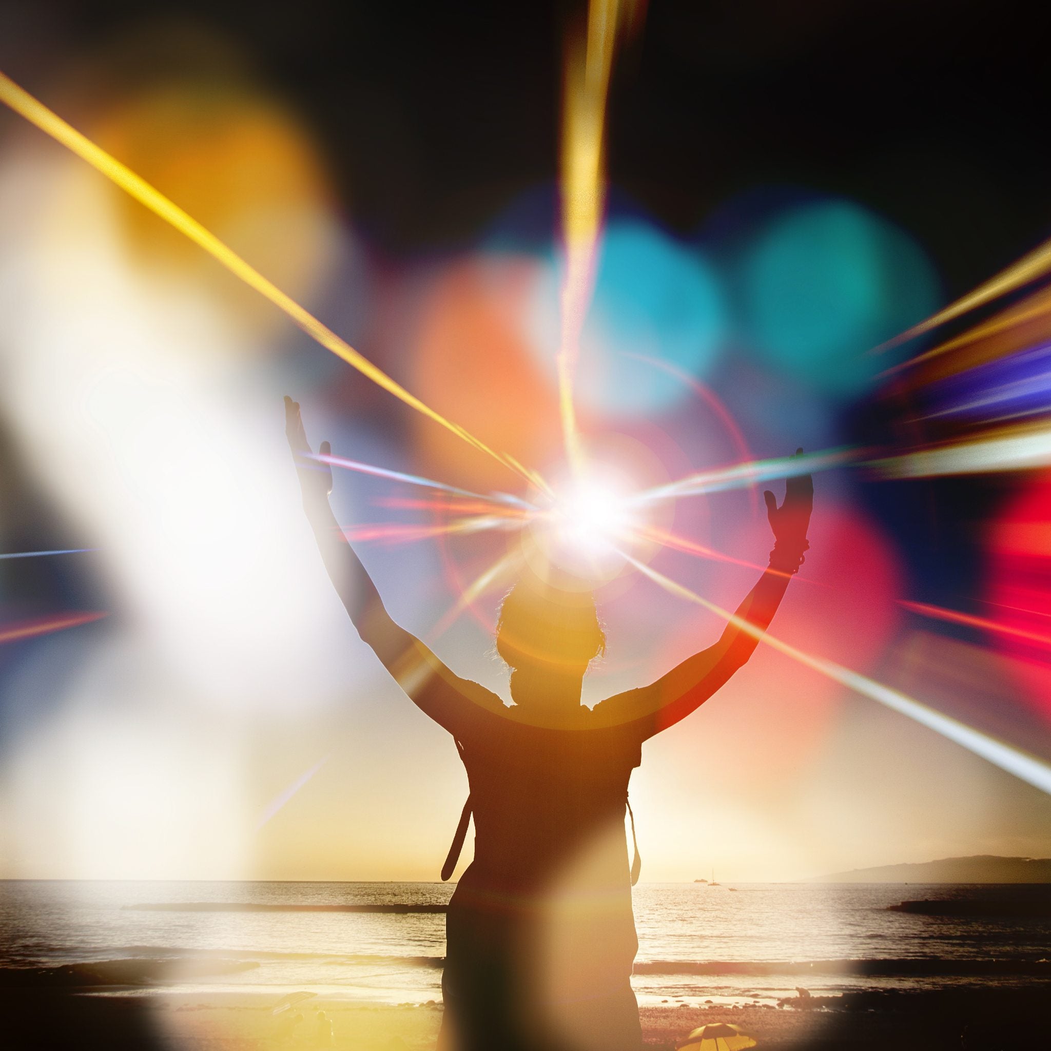 A silhouette of a person standing on a beach with arms raised to the sky, surrounded by bright, colourful streaks of light and bokeh spheres, with an intense light emanating from their head, symbolising spiritual awakening.
