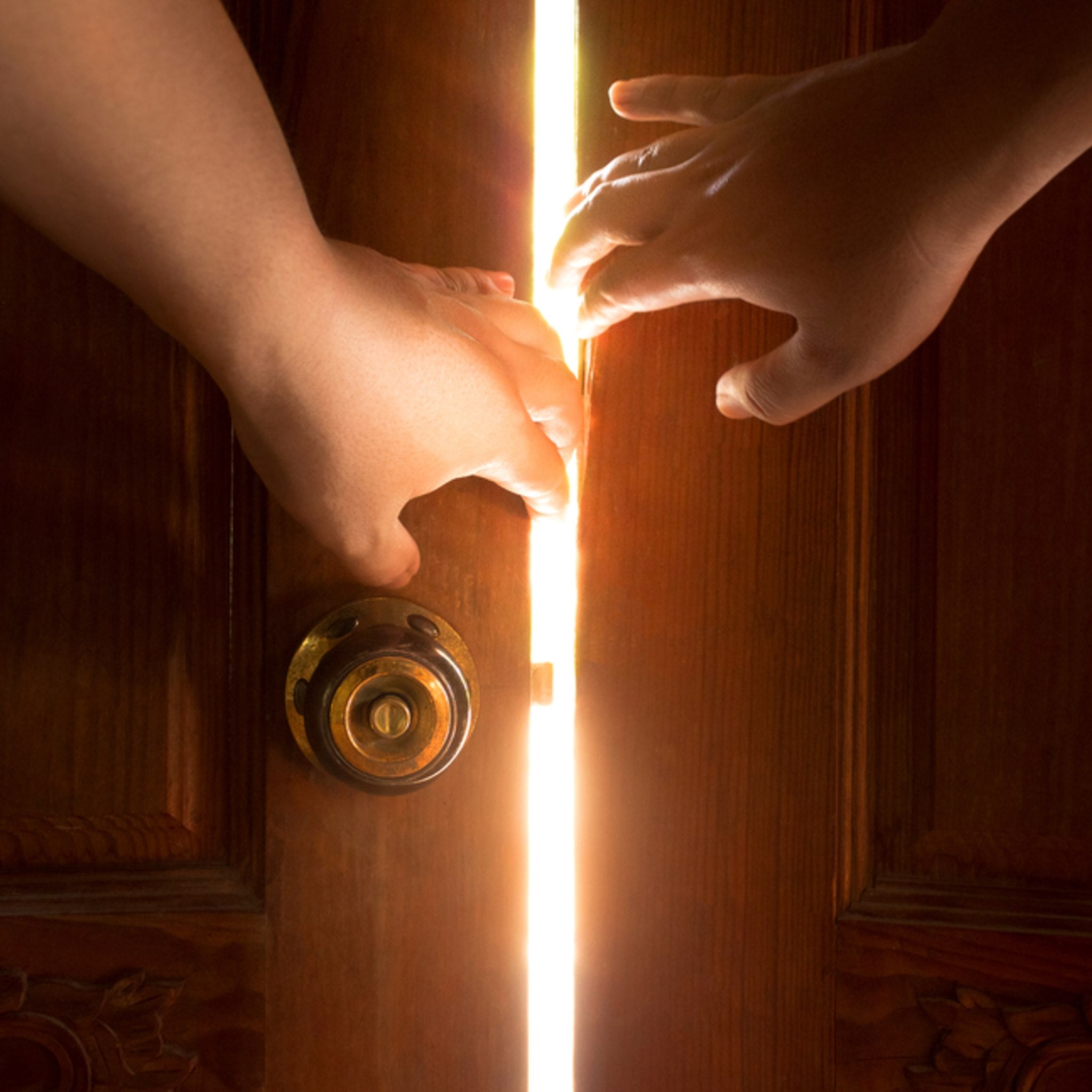 A stylised image of two hands reaching towards a wooden door with radiant light streaming through, pushing away dark. Symbolises energetic clearing, purification, obstacle removal, and spiritual light.