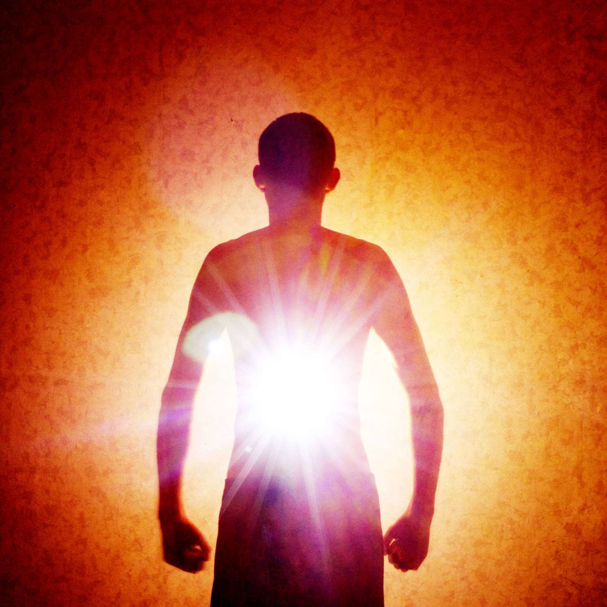 A dark silhouette of a person standing against a grainy, orange and red background. A brilliant, star-shaped burst of white light emanates from the centre of the person's chest, signifying the core star or higher heart chakra.