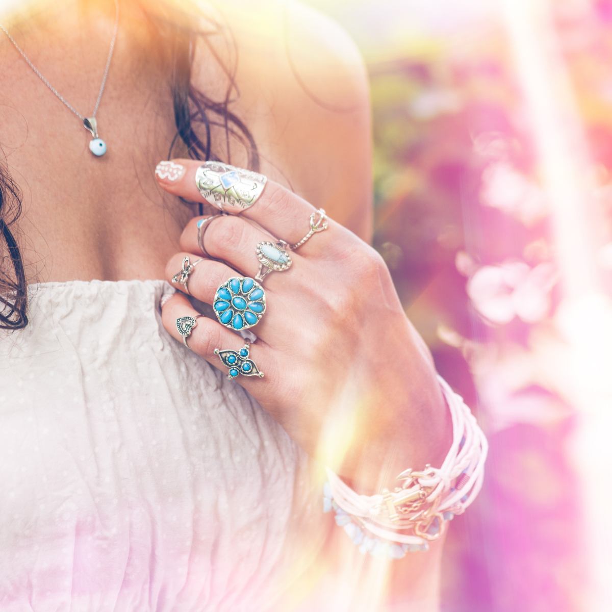 A close-up of a woman's hand with rings and a pink light background.