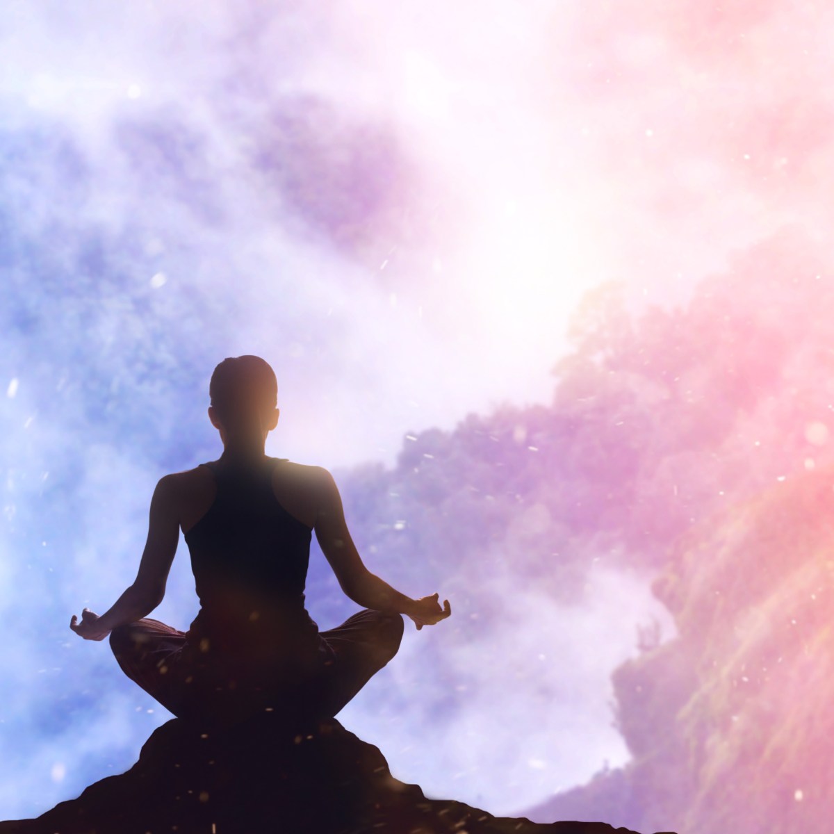 Silhouette of a person meditating against a colourful, pink cloudy sky background.