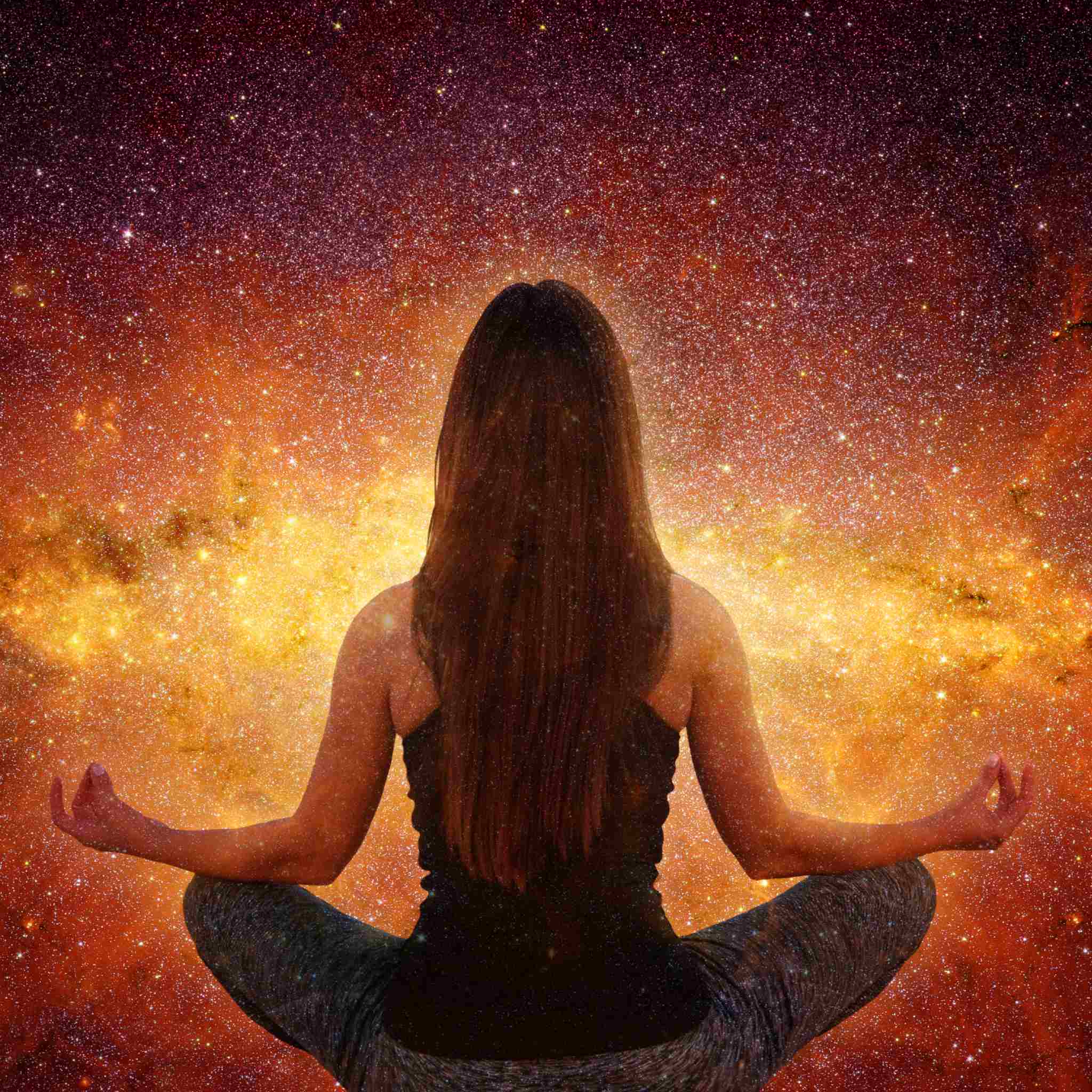 A woman in a black tank top and yoga pants sits in a meditating pose, viewed from behind, set against a stunning, vibrant, golden-orange nebula and starry celestial background.