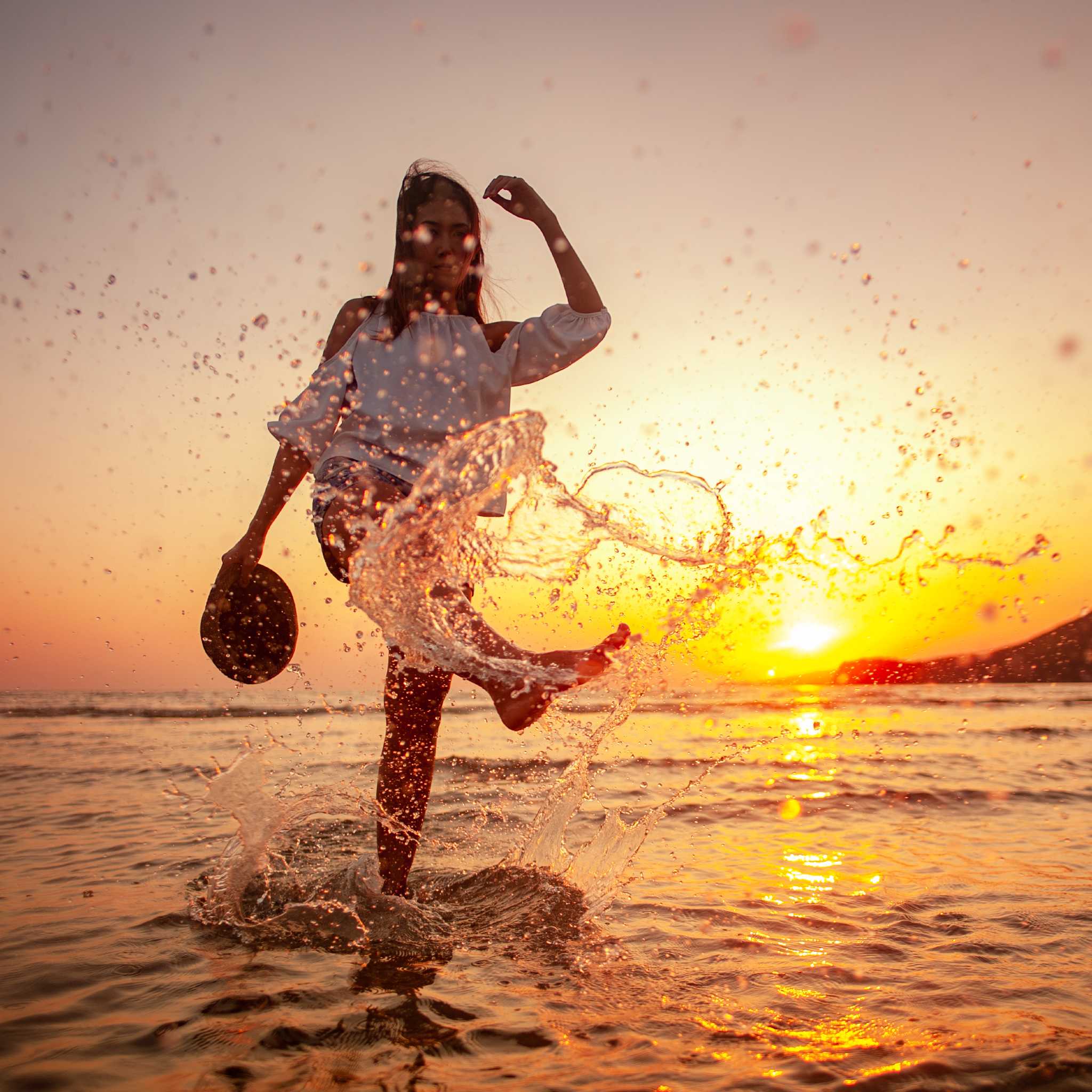 A silhouette of a woman splashing water with her foot at sunset on a beach, representing the powerful energy of Artemis connections.
