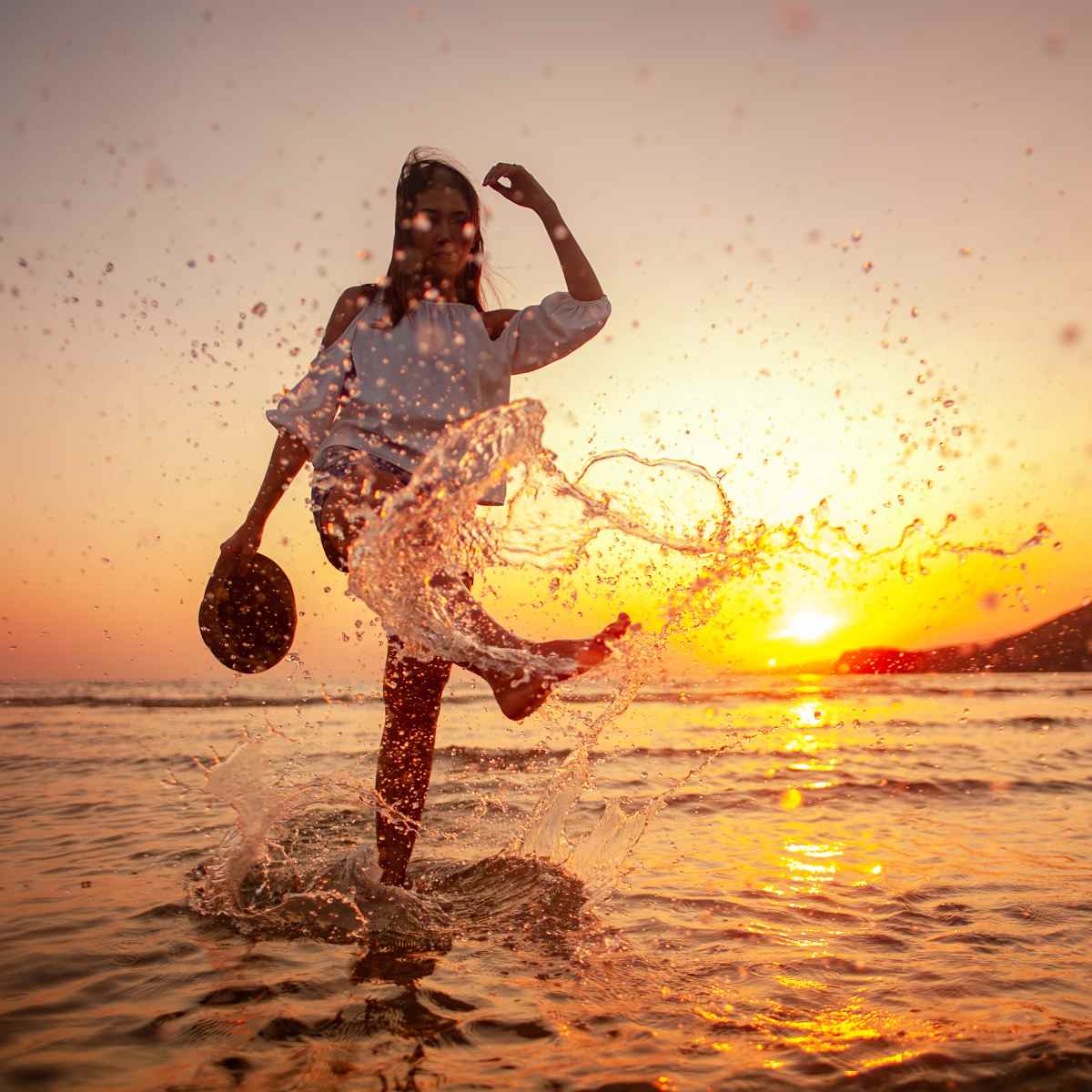 A silhouette of a woman splashing water with her foot at sunset on a beach, representing the powerful energy of Artemis connections.
