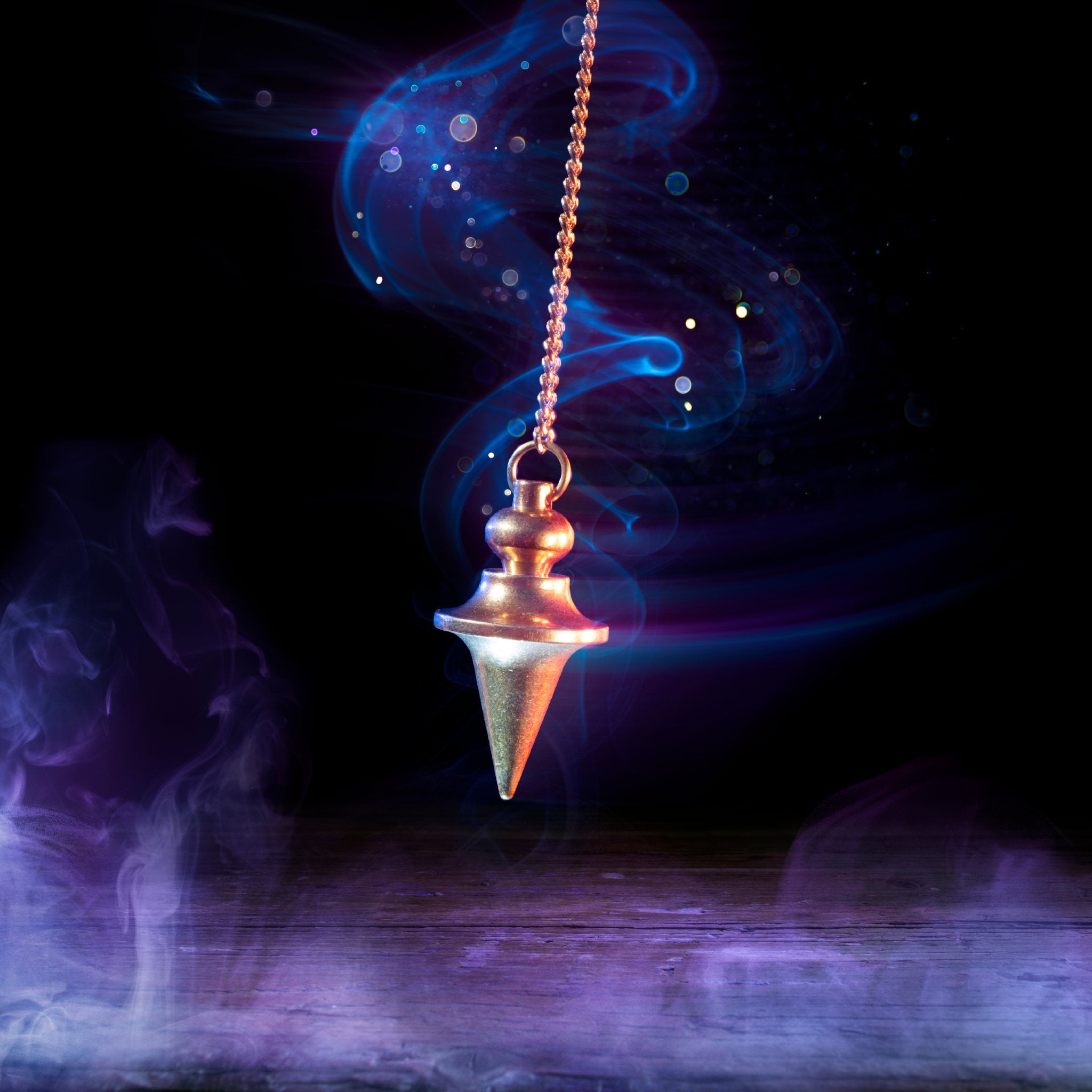 A brass pendulum, hanging from a chain, hovers over a dark wooden surface, surrounded by wisps of ethereal blue and purple smoke and glowing particles against a black background.