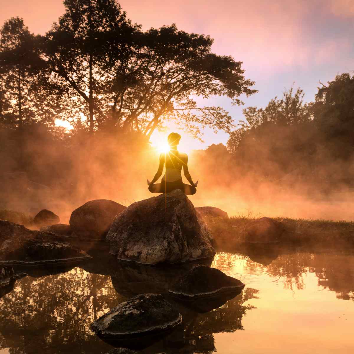 Person meditating on a rock by a lake at sunset with a misty atmosphere.