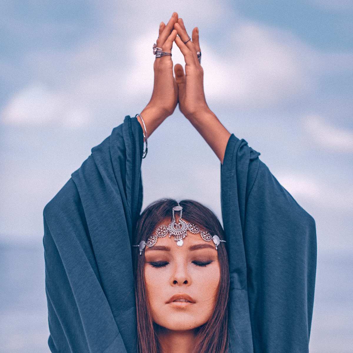 A serene woman with eyes closed, raises her hands in offering above her head with harmonious energy.
