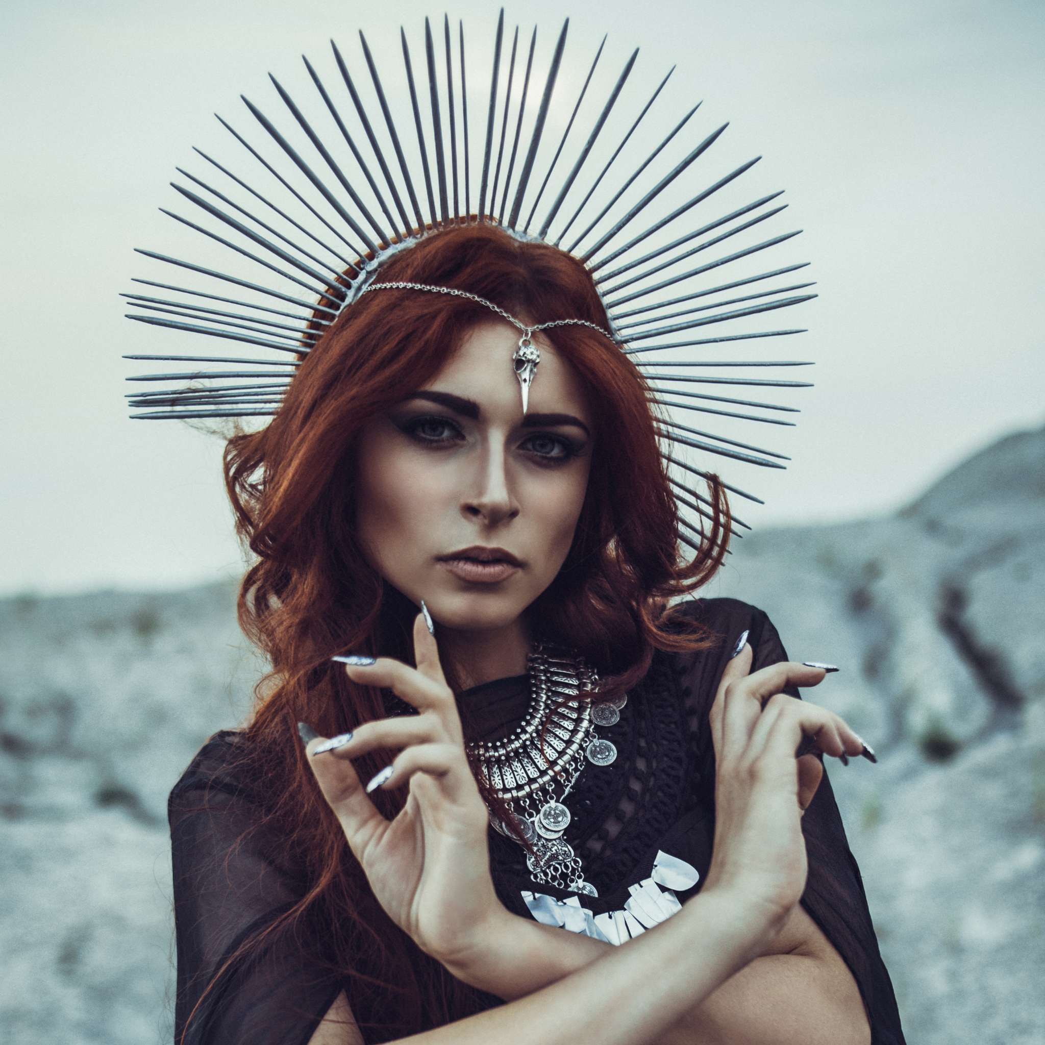 Woman with red hair and intricate headpiece against a rocky background representing Hecate.