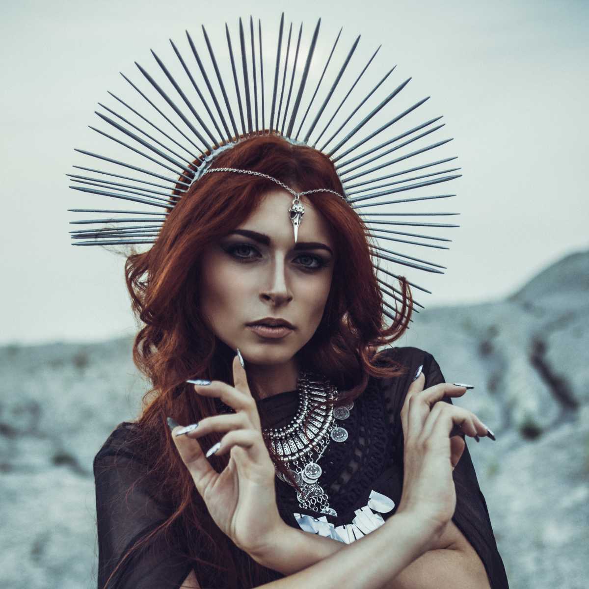 Woman with red hair and intricate headpiece against a rocky background representing Hecate.