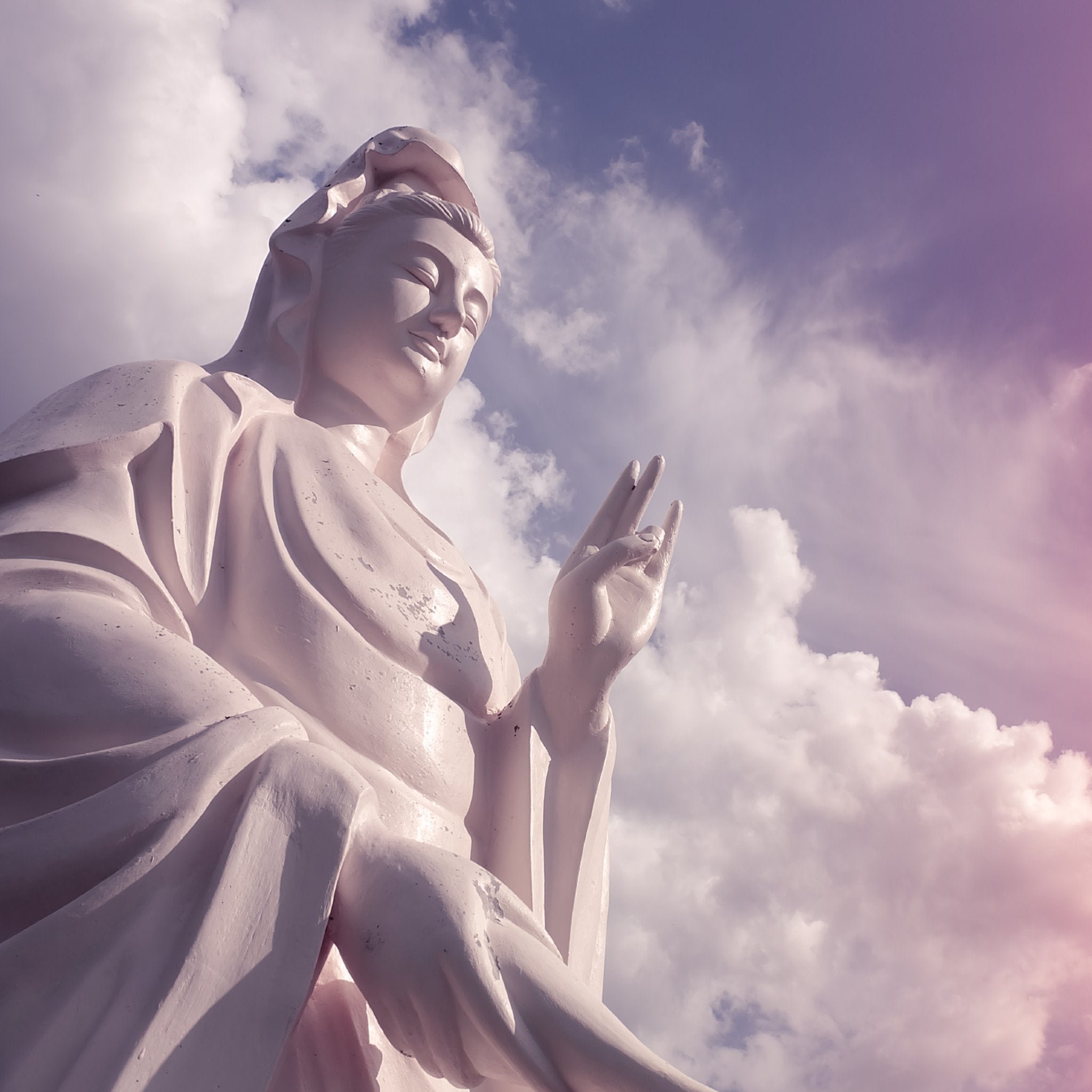 A large white statue of Kuan Yin (Goddess of Compassion) set against a soft, cloudy sky, representing Kuan Yin connections.