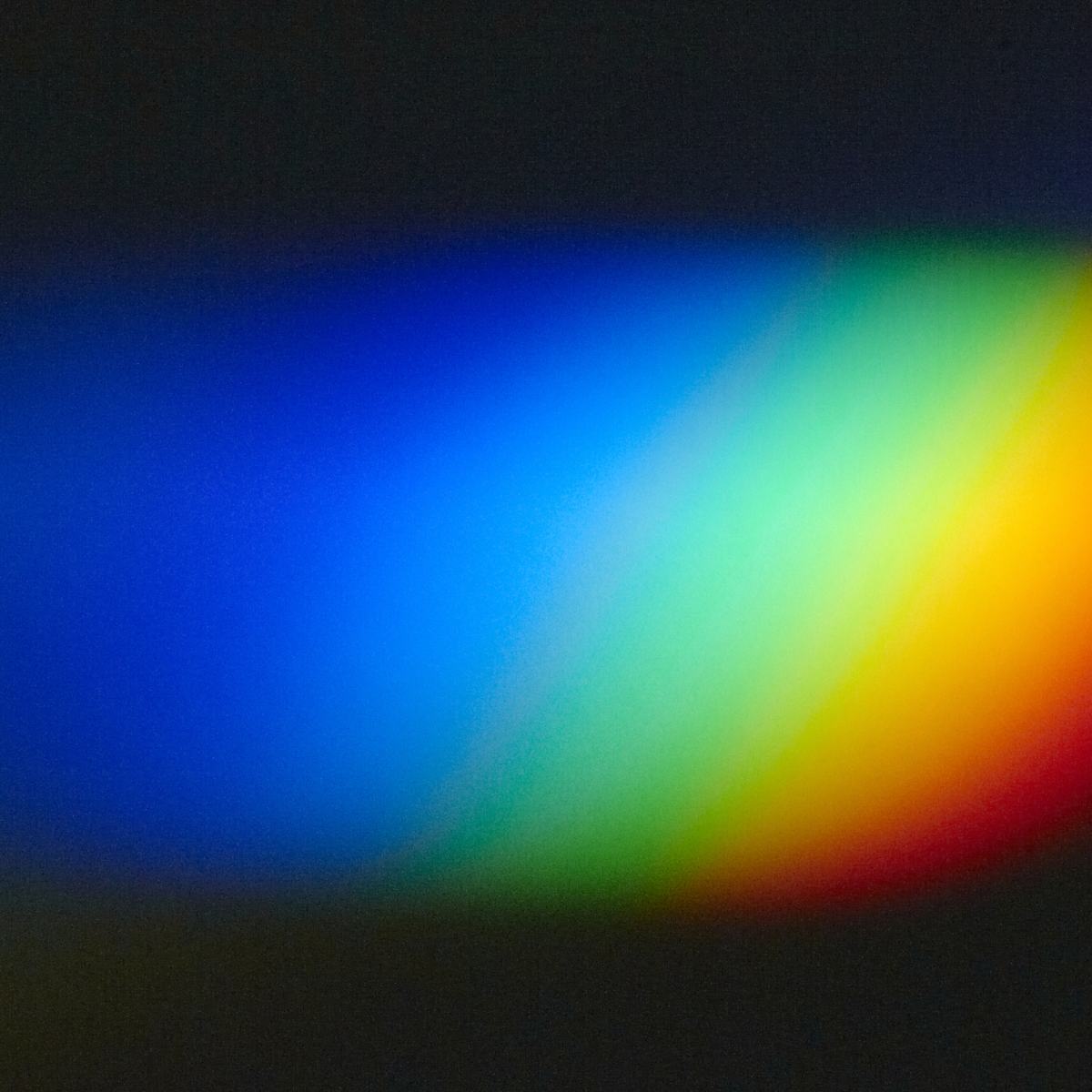 A vibrant rainbow light spectrum refraction with soft, blurry gradients blending across a dark, grainy background.
