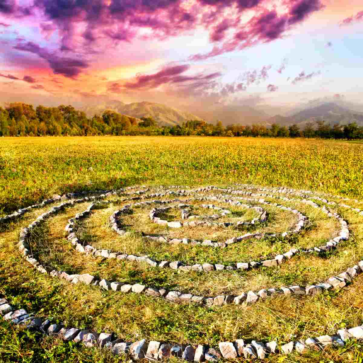 A medicine wheel or labyrinth with a vibrant sunset over distant hills and forest in the background.