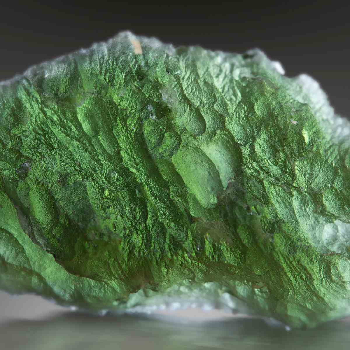 Close-up of a moss green Moldavite crystal with a dark background.