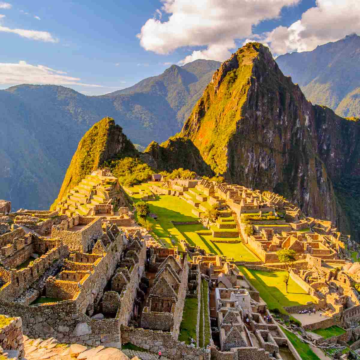 A wide-angle view of the ancient sacred site of Machu Picchu nestled between green peaks under a blue sky.