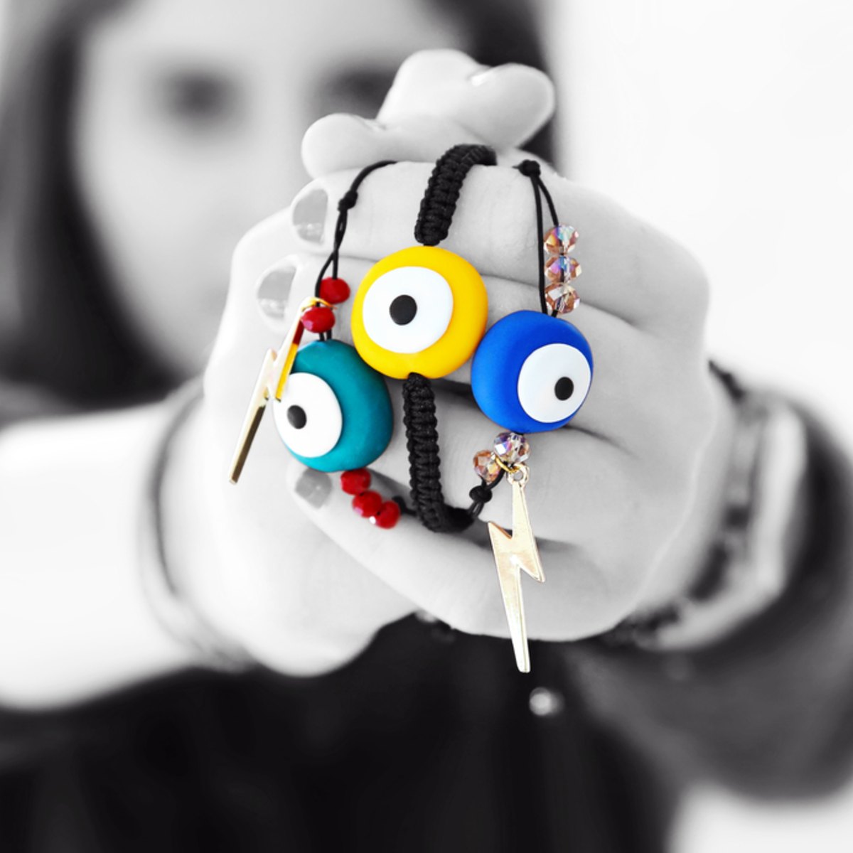A person holding outstretched arms holding colourful evil eye charms on a white background.