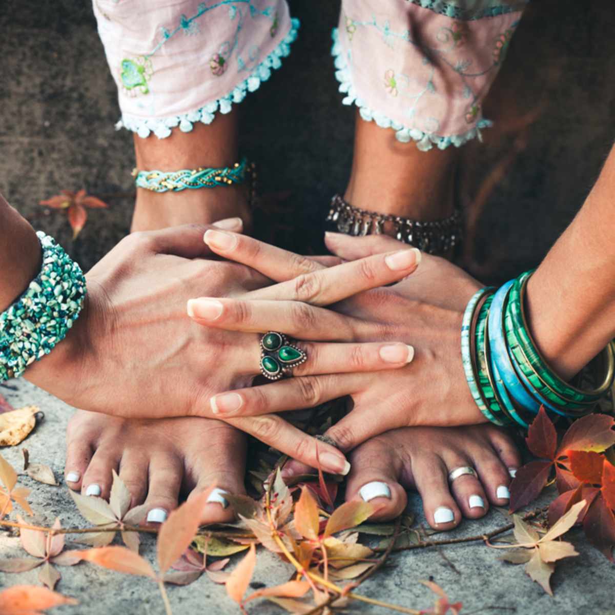 Close-up of bare feet with a green ring and colourful bracelets standing on the ground, grounding on a natural background.