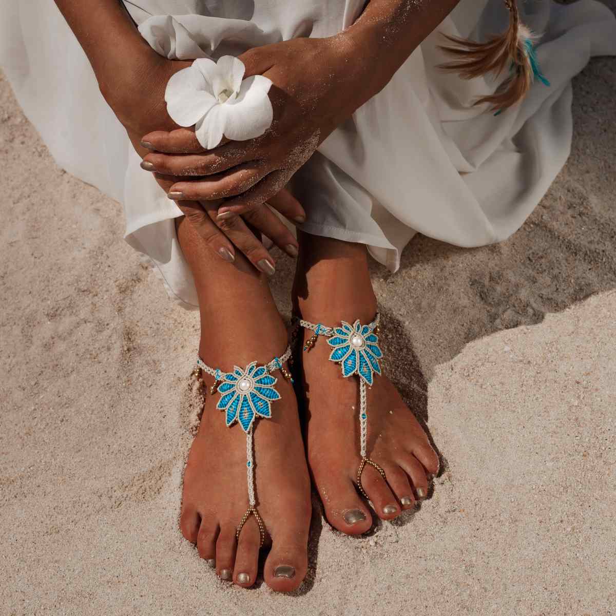 Close-up of feet wearing decorative anklets on a sandy background.
