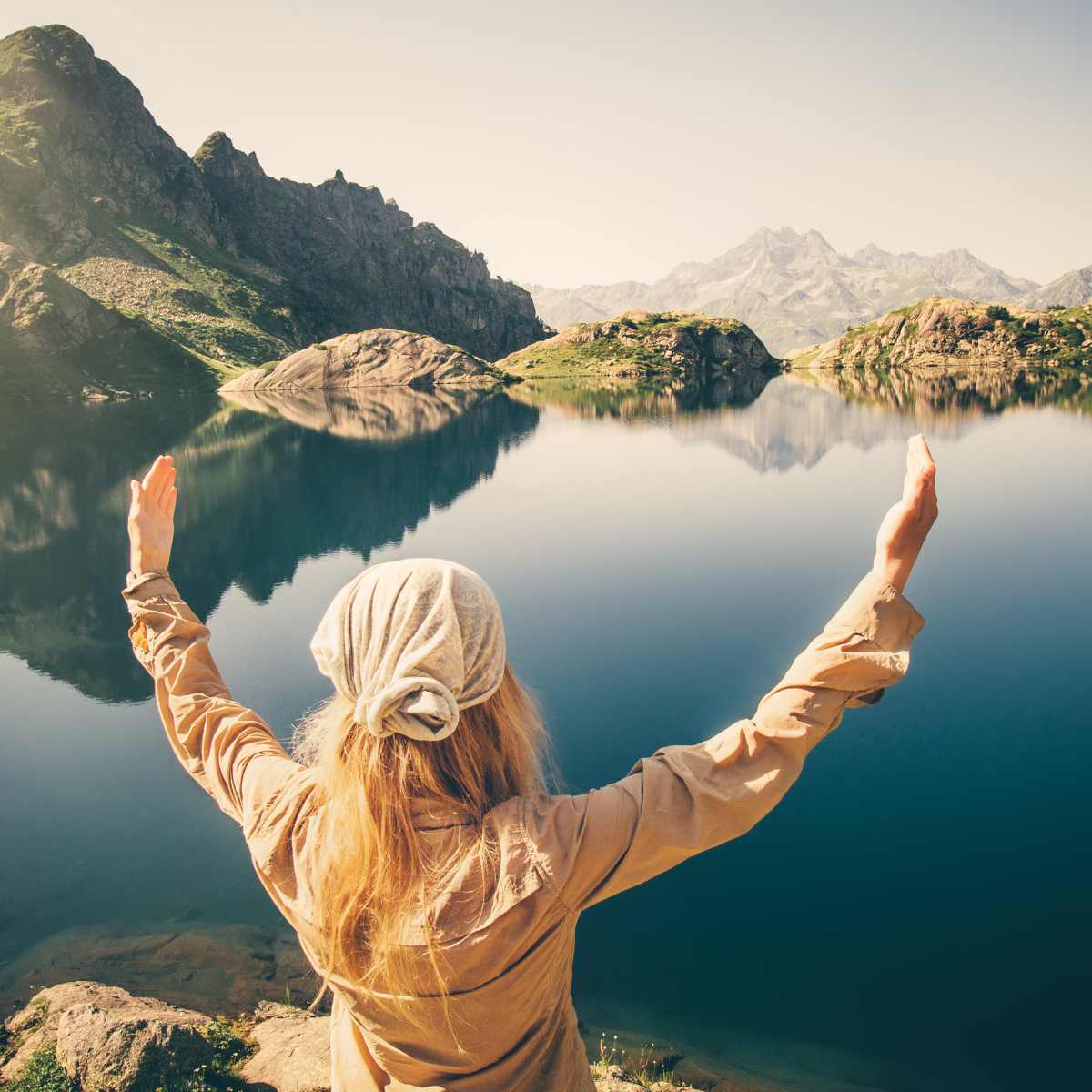 Person with arms outstretched overlooking a serene lake and mountains.
