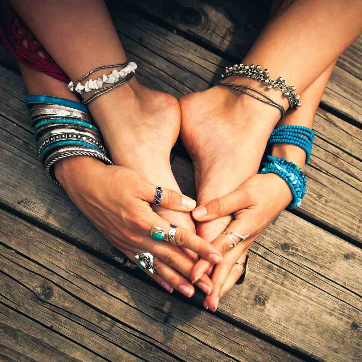 A close-up of a person's bare feet and hands adorned with many silver and blue bracelets signifying grounding.