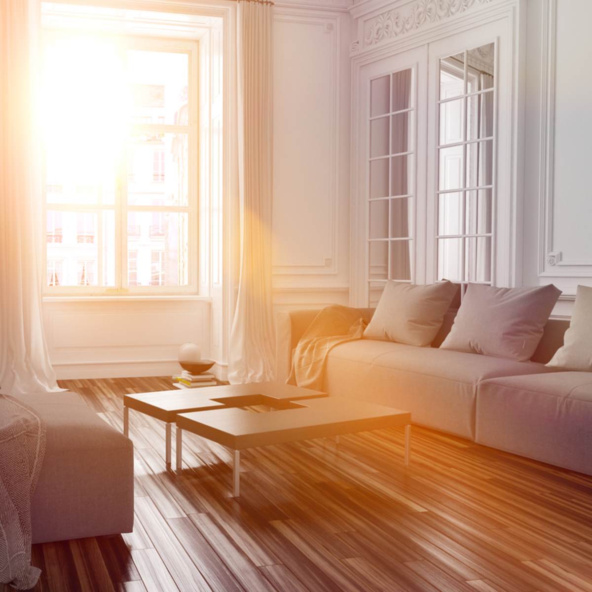 Brightly lit living room with a white sofa, wooden coffee table, and large windows.