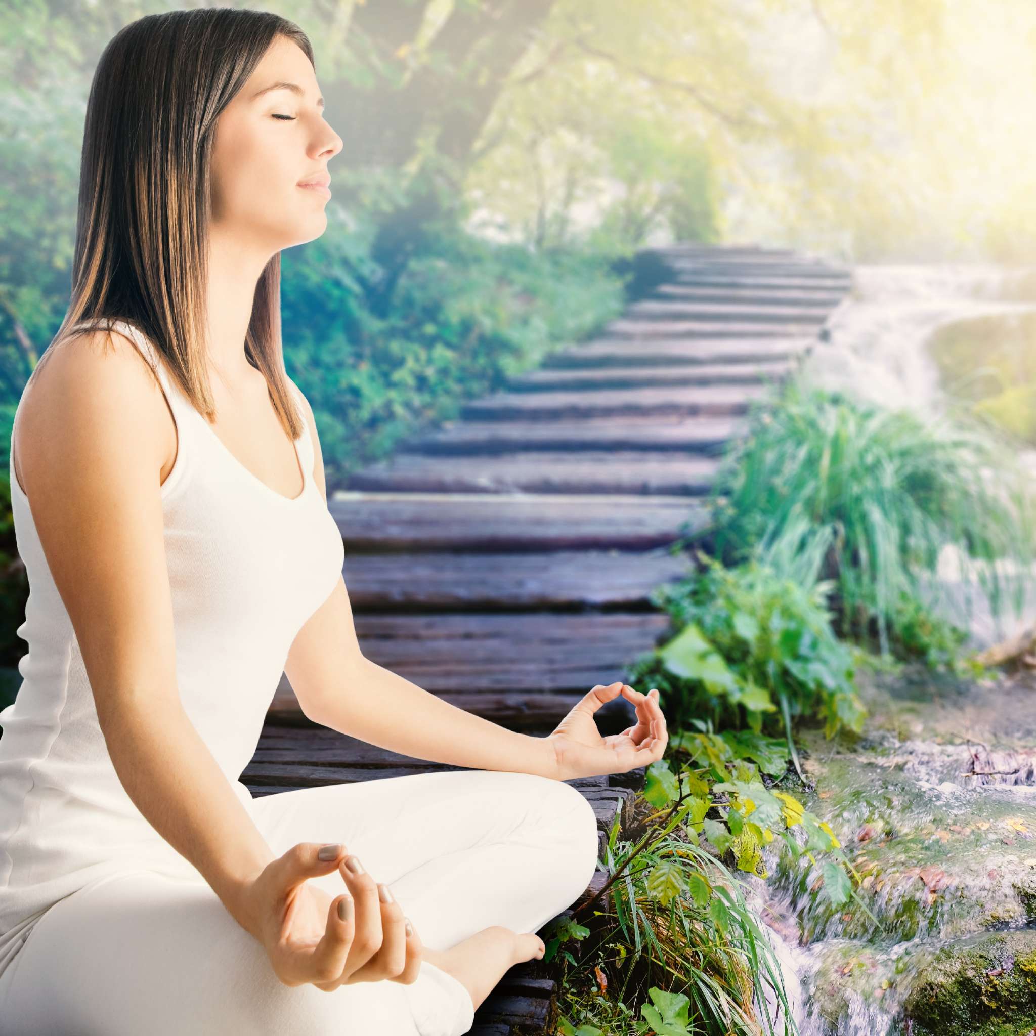 A woman meditating outdoors on a wooden platform over a waterfall in a sunny, green setting, representing the focused intention rite.