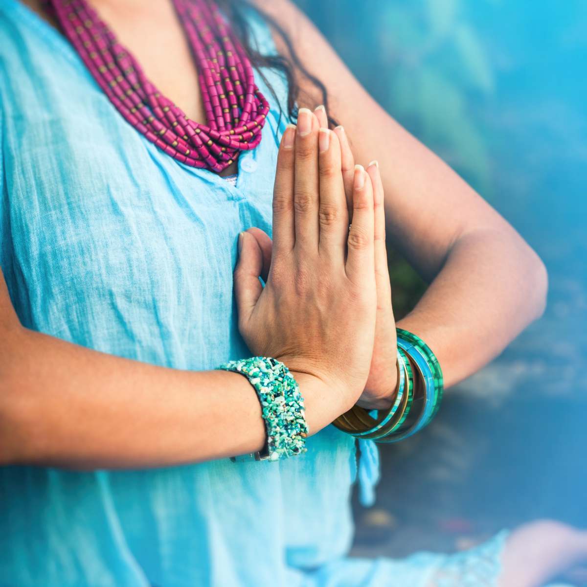 Kundalini Reiki Master Teacher attunement course featuring a close-up of a person sitting cross-legged with hands in prayer position wearing bohemian jewellery.
