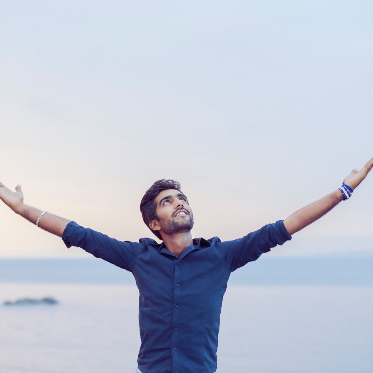 An inspired man with arms outstretched against a clear sky.