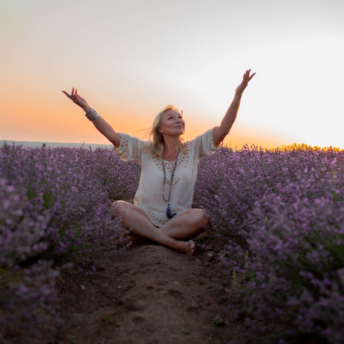Woman sitting cross-legged in a purple lavender field at sunset representing manifestation path alignment dedication.