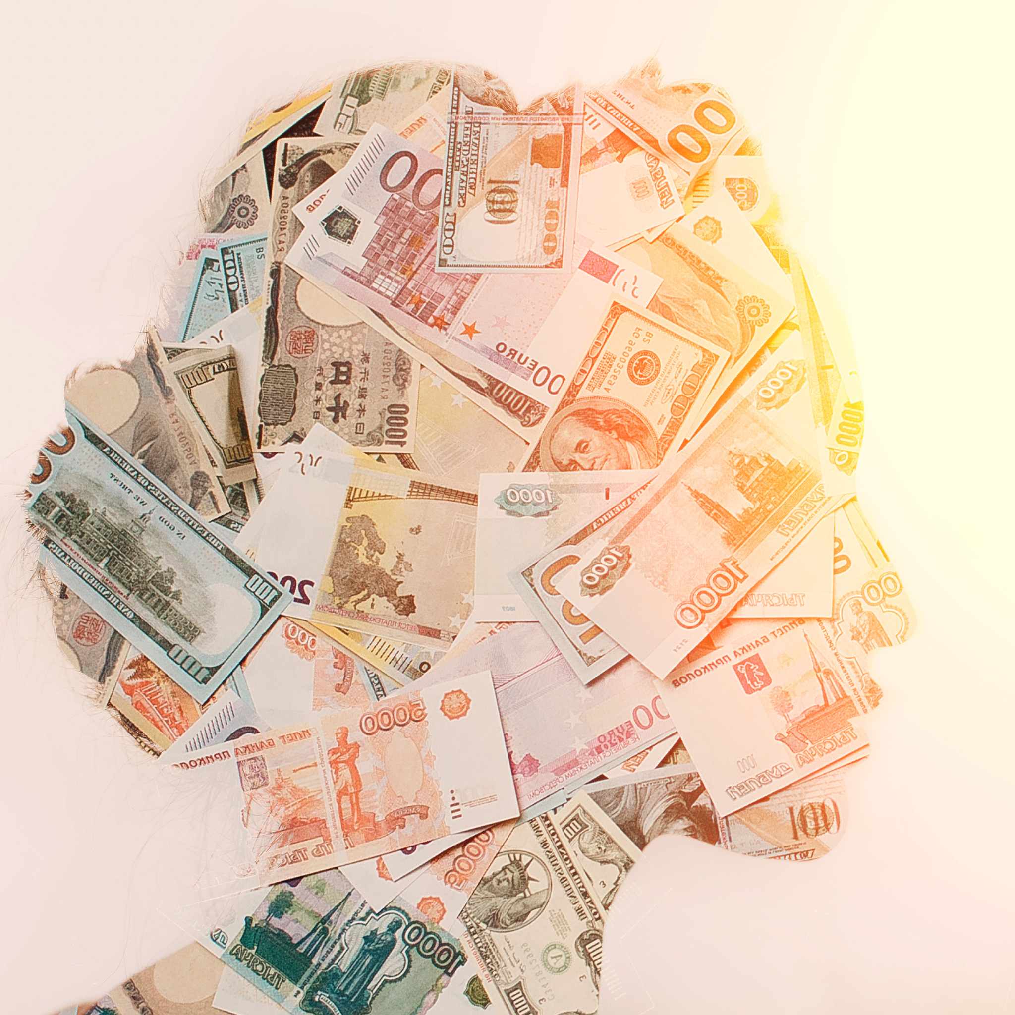 A silhouette of a human head filled with a collage of various international paper currencies, illuminated by a bright, warm light.