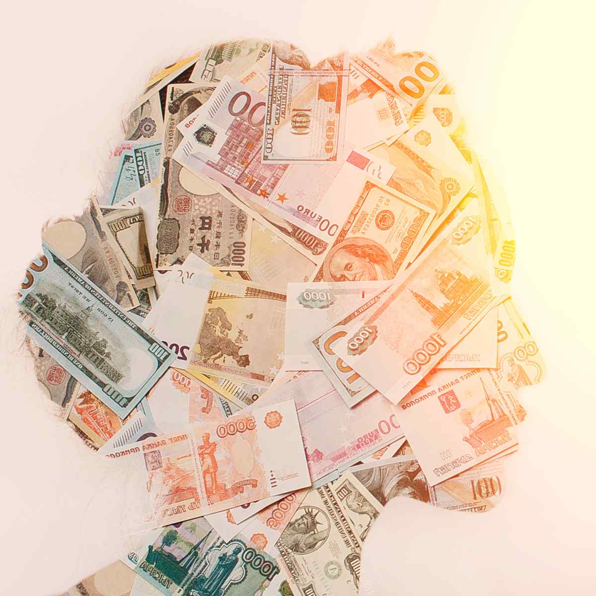 A silhouette of a human head filled with a collage of various international paper currencies, illuminated by a bright, warm light.