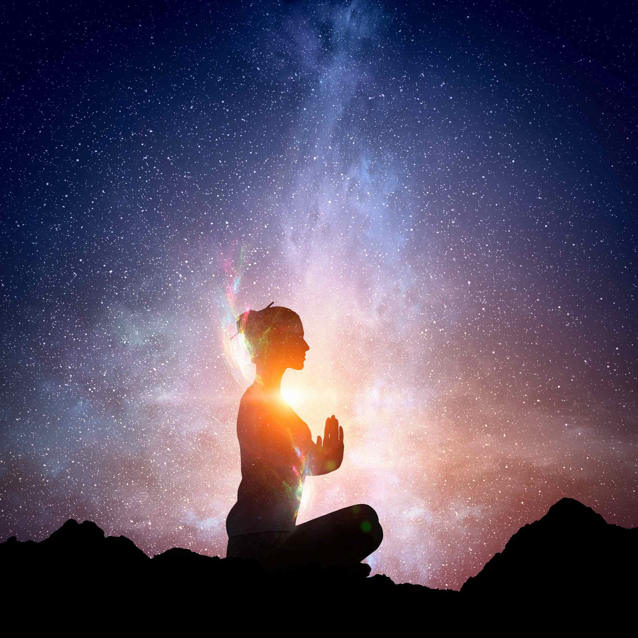 A dark silhouette of a person sitting in the lotus position on a rocky horizon line, meditating with hands pressed together in a prayer pose. The figure is brightly backlit by an intense orange light on the horizon, contrasting with a deep blue, starry cosmic sky above the milky way.