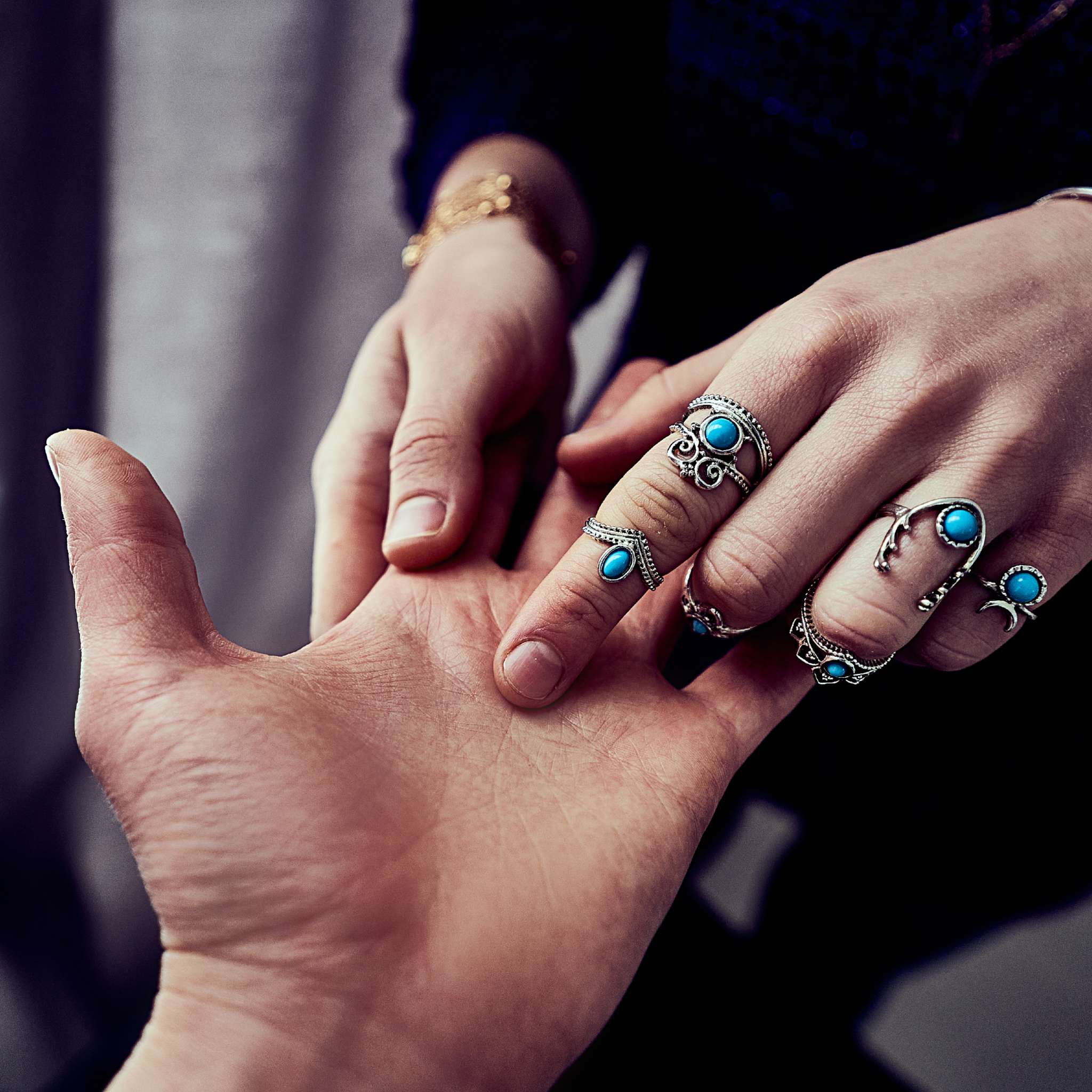 A close-up photograph of a palmist wearing several ornate silver rings with turquoise stones, gently touching and tracing a line on another person's open palm. This ritualistic gesture signifies the act of reading the future through the lines of the hand, representing the focus of the palmist path alignment dedication.
